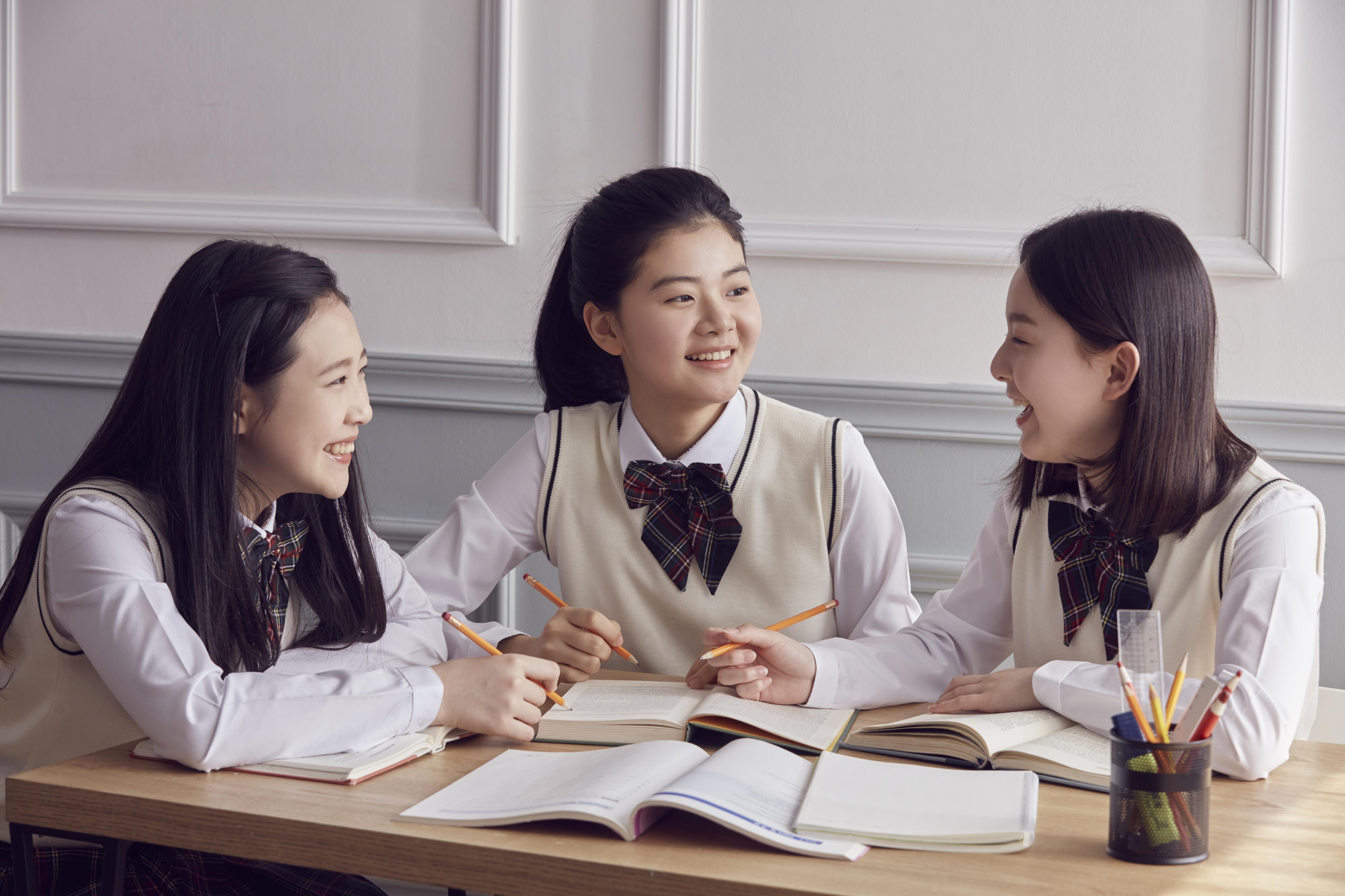 교재를 펼쳐 대화하는 세 학생 · 시험 준비 참고 사진